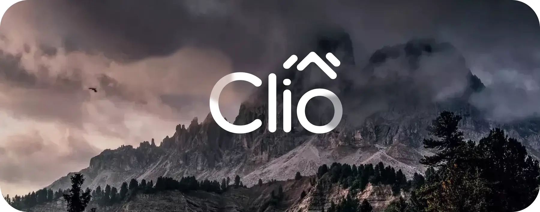 Moody mountain landscape with dark clouds and a flying bird, overlaid with the text "Cliô" in white. Trees dot the rugged terrain, adding a natural feel to the scene, perfectly capturing the essence of Cliô websites and their serene aesthetic. - Clio Websites | Top Canadian Web Design Company