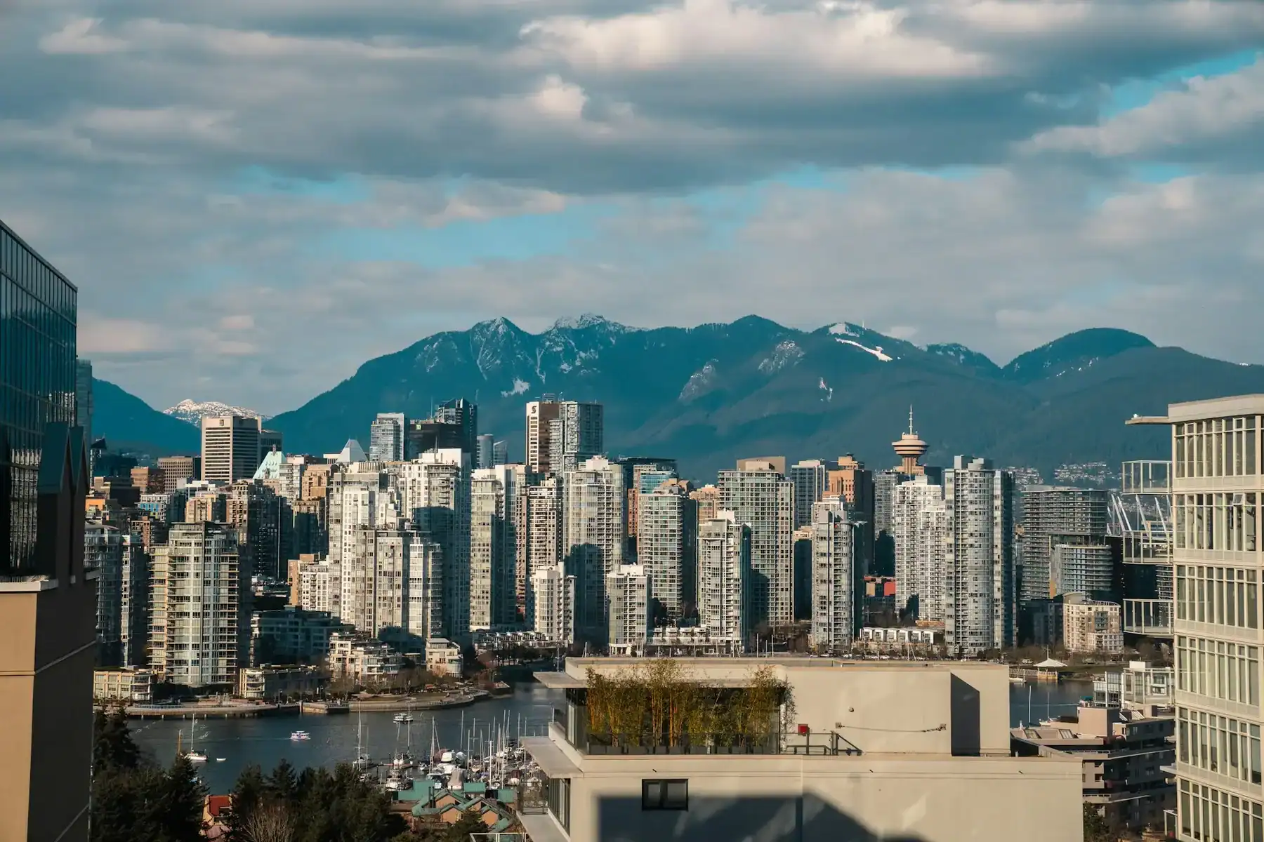 A city skyline with tall buildings, a harbor, and mountains in the background under a partly cloudy sky—an inspiring scene reminiscent of the creativity that fuels Saskatoon web design and innovative WordPress development in Saskatoon. - Clio Websites | Top Canadian Web Design Company