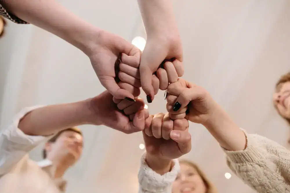 Five people join their fists together in a circle, forming a united gesture, viewed from below. Their faces are partially visible, and the softly lit background evokes a sense of collaboration—a perfect visual metaphor for membership web design. - Clio Websites | Top Canadian Web Design Company
