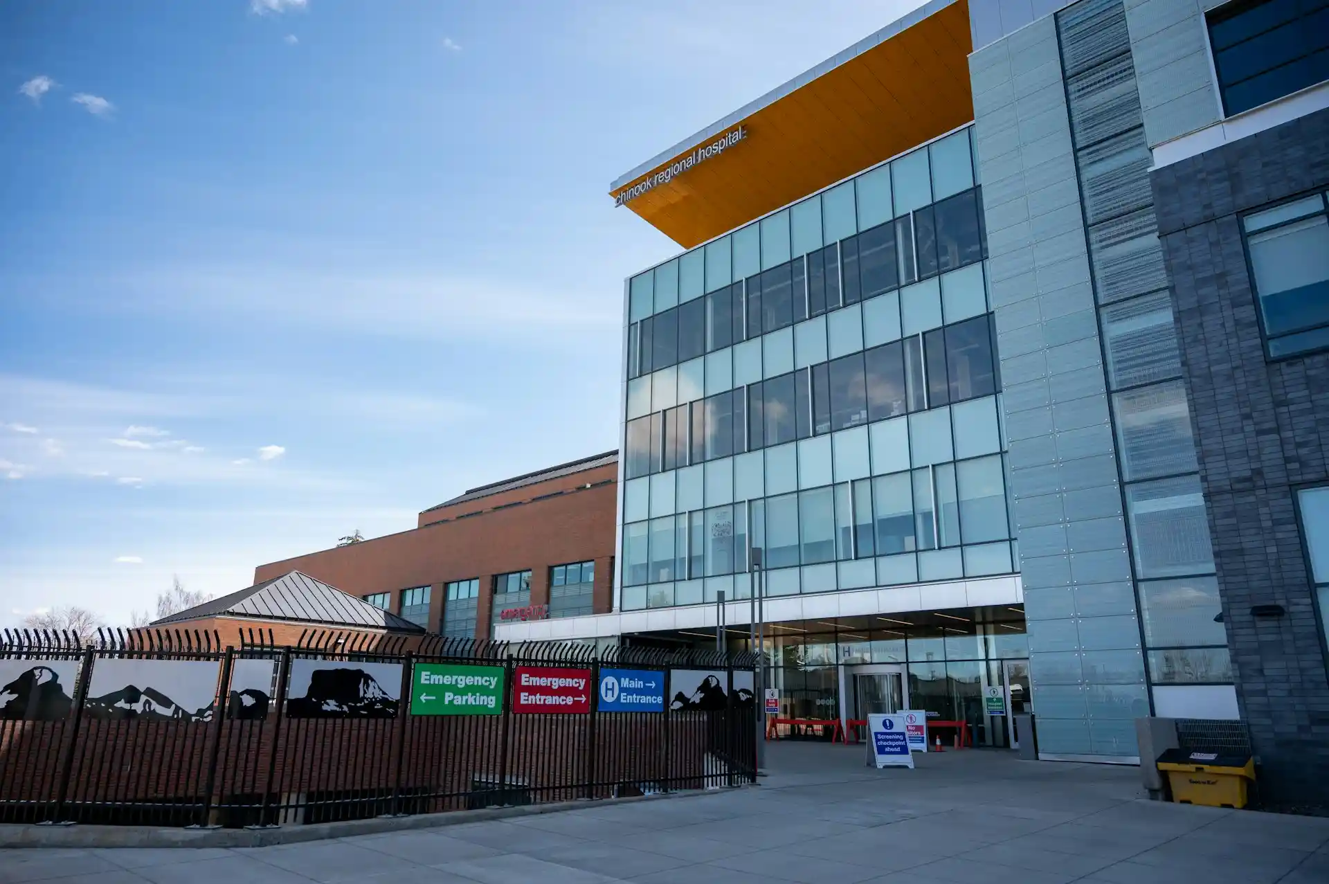 A modern hospital building with glass windows stands prominently, its signs indicating emergency entrance and parking. The sky is clear, and the area outside appears clean and well-maintained, reflecting the attention to detail found in a top Saskatoon web design company. - Clio Websites | Top Canadian Web Design Company
